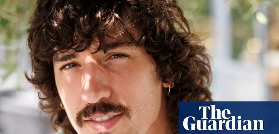 Hombre con cabello rizado y bigote sonriendo