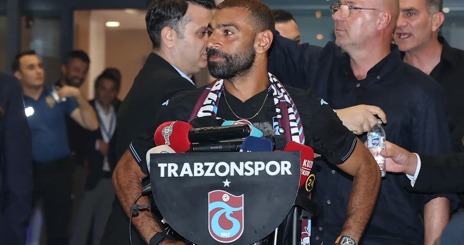 Jugador en rueda de prensa con micrófonos y escudo de Trabzonspor