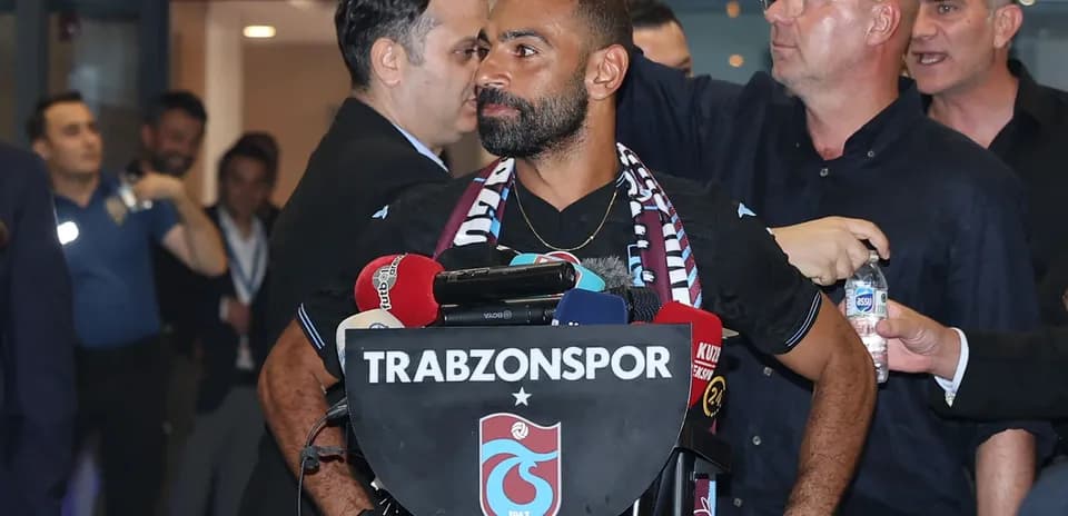 Jugador en rueda de prensa con micrófonos y escudo de Trabzonspor