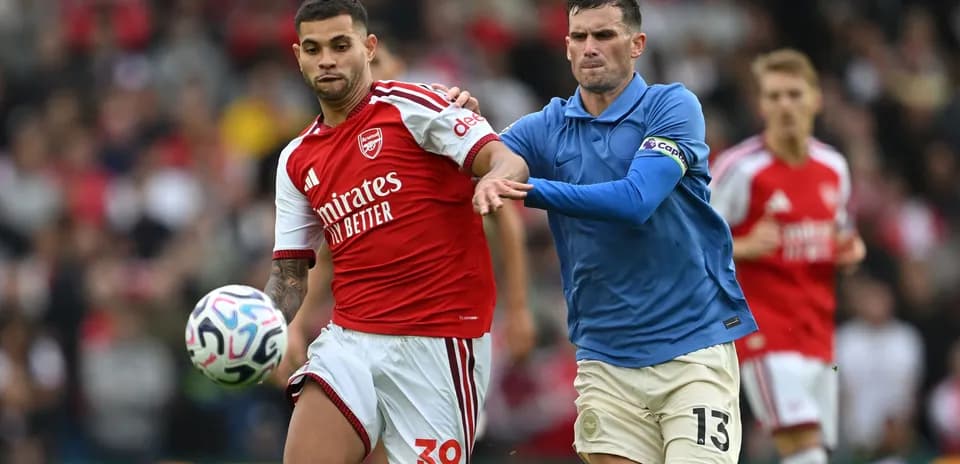 Jugador de Arsenal controlando el balón, rival persiguiéndolo
