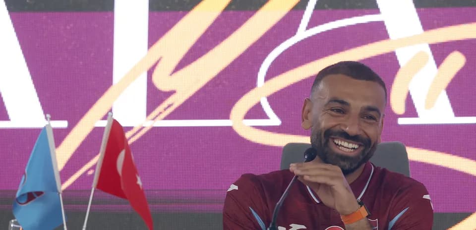Jugador sonriendo en conferencia de prensa con banderas