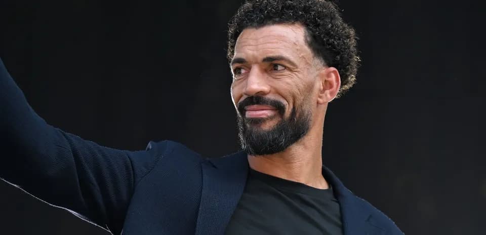 Hombre con barba y cabello rizado saludando al público
