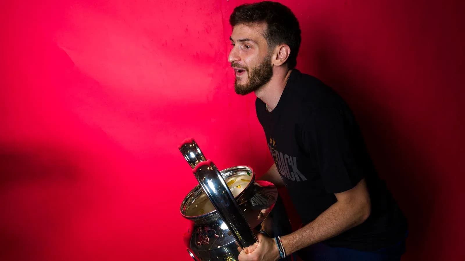 Jugador sosteniendo un trofeo frente a fondo rojo
