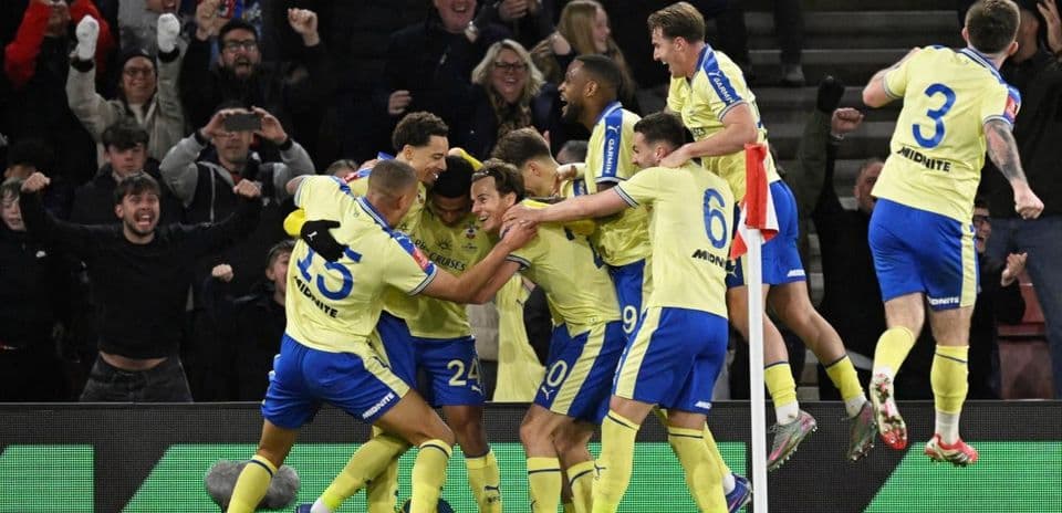 Jugadores celebrando un gol rodeados de aficionados