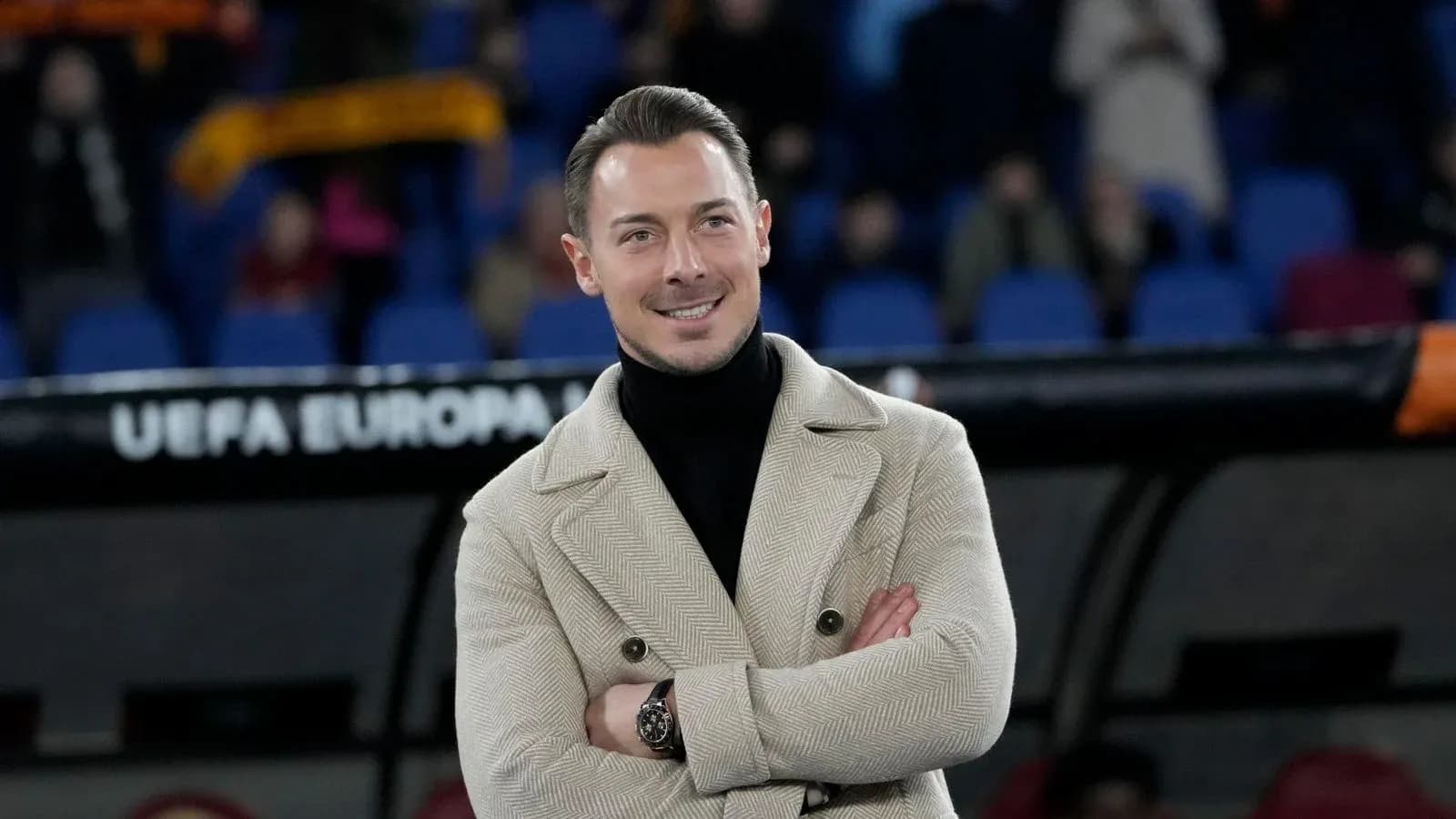 Hombre sonriente con abrigo en un estadio