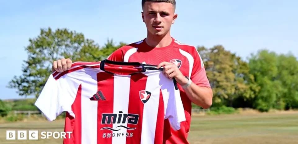 Jugador sosteniendo camiseta de Cheltenham Town en campo