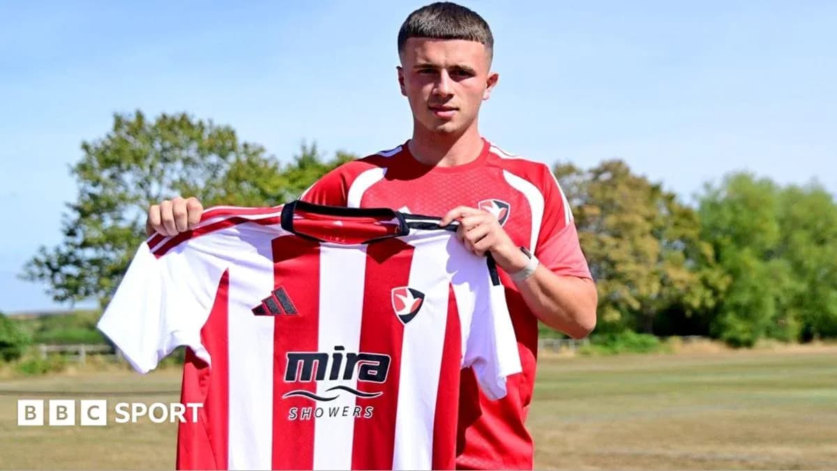 Jugador sosteniendo camiseta de Cheltenham Town en campo