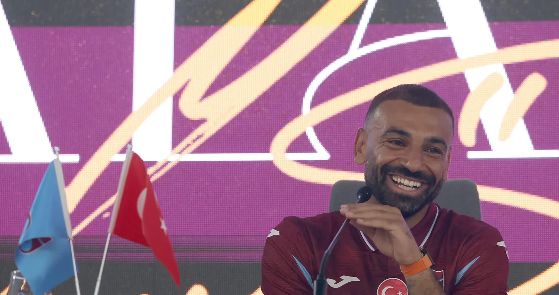Jugador sonriendo en conferencia de prensa con banderas Jugador sonriendo en conferencia de prensa con banderas