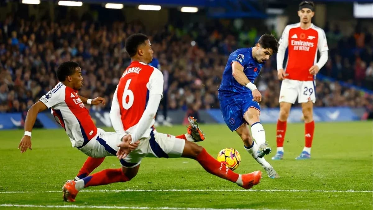 Jugador de Chelsea disparando mientras dos defensores de Arsenal intentan detenerlo Jugador de Chelsea disparando mientras dos defensores de Arsenal intentan detenerlo